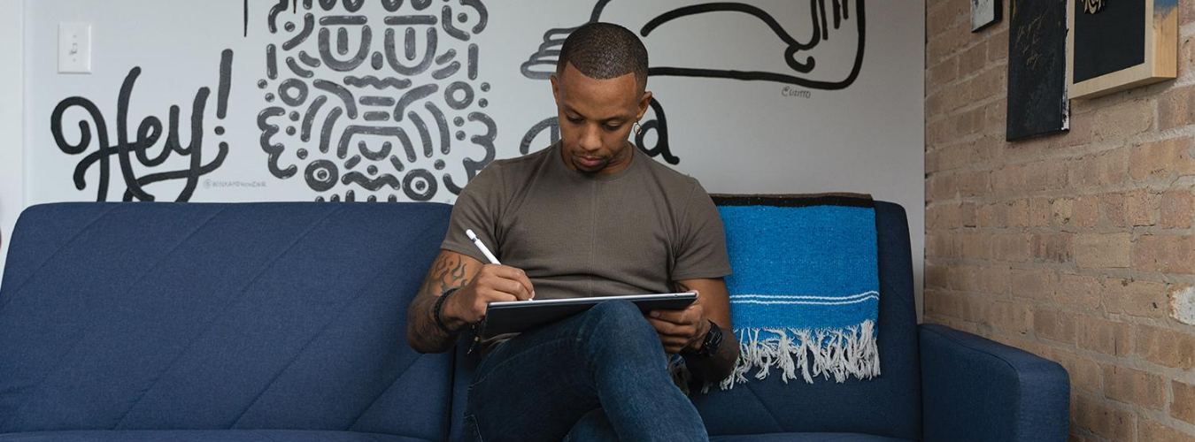 male sitting on a couch with handwritten typeography on the walls, holding a notepad and pen