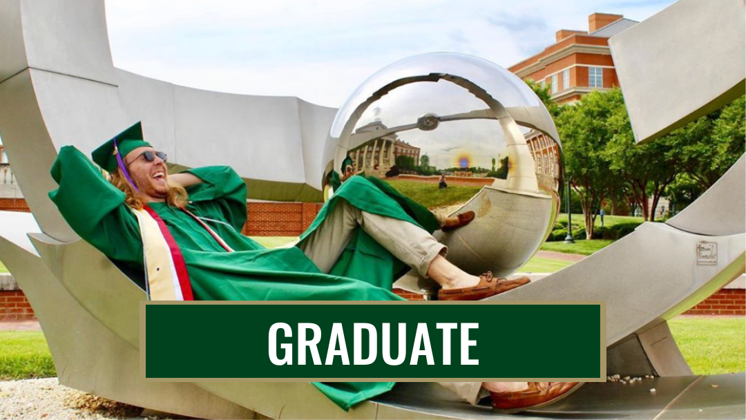 grad student in his cap an gown sitting on a sculpture on campus with a big smile on his face