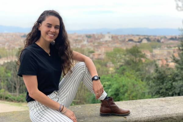 photo of recent graduate sitting with the view of a city behind her