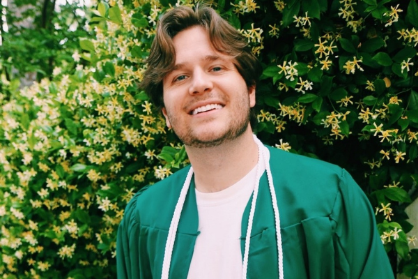 photo of recent graduate in cap and gown in front of a flower bush