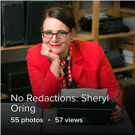 woman in a red blazer and glasses with her hand propping up her face. showing a soft smile 