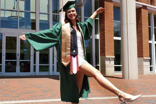 photo of recent graduate in cap and gown in front of robinson hall