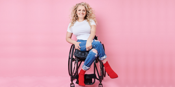 a woman with blond hair wearing red boots sitting in a wheel chair against a soft pink background